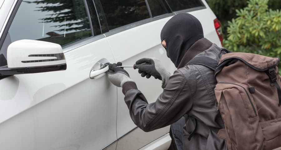 Thief attempting to break into a white vehicle in a residential setting